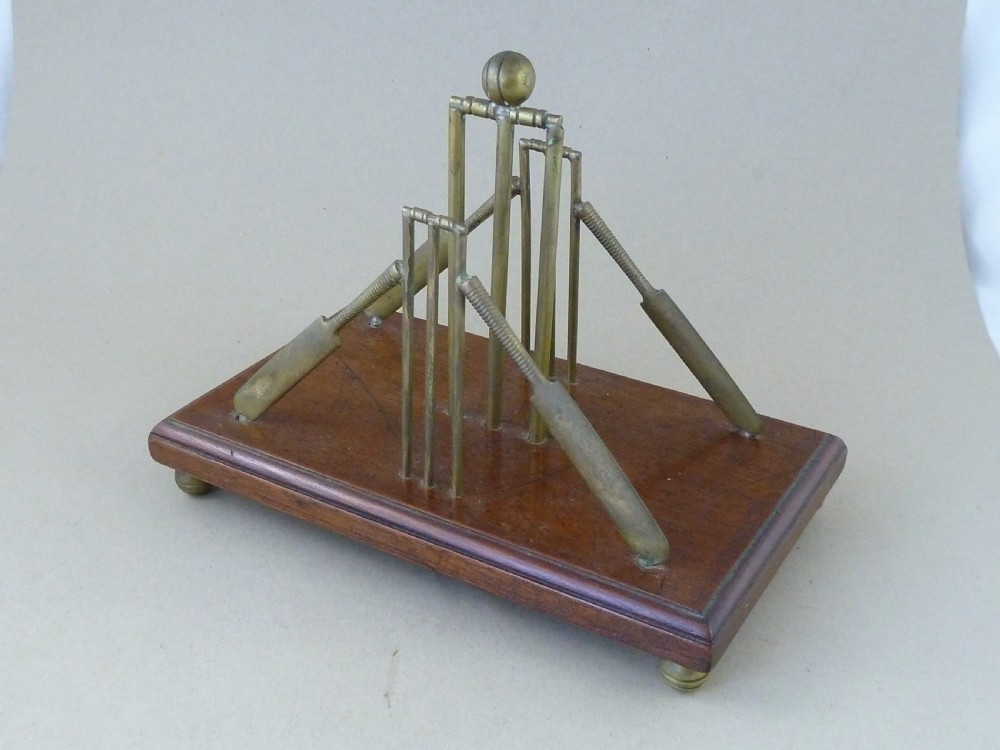 An antique brass letter rack shaped as miniature cricket bats, wickets, and a ball mounted on a rectangular mahogany wooden base with small bun feet. View IX