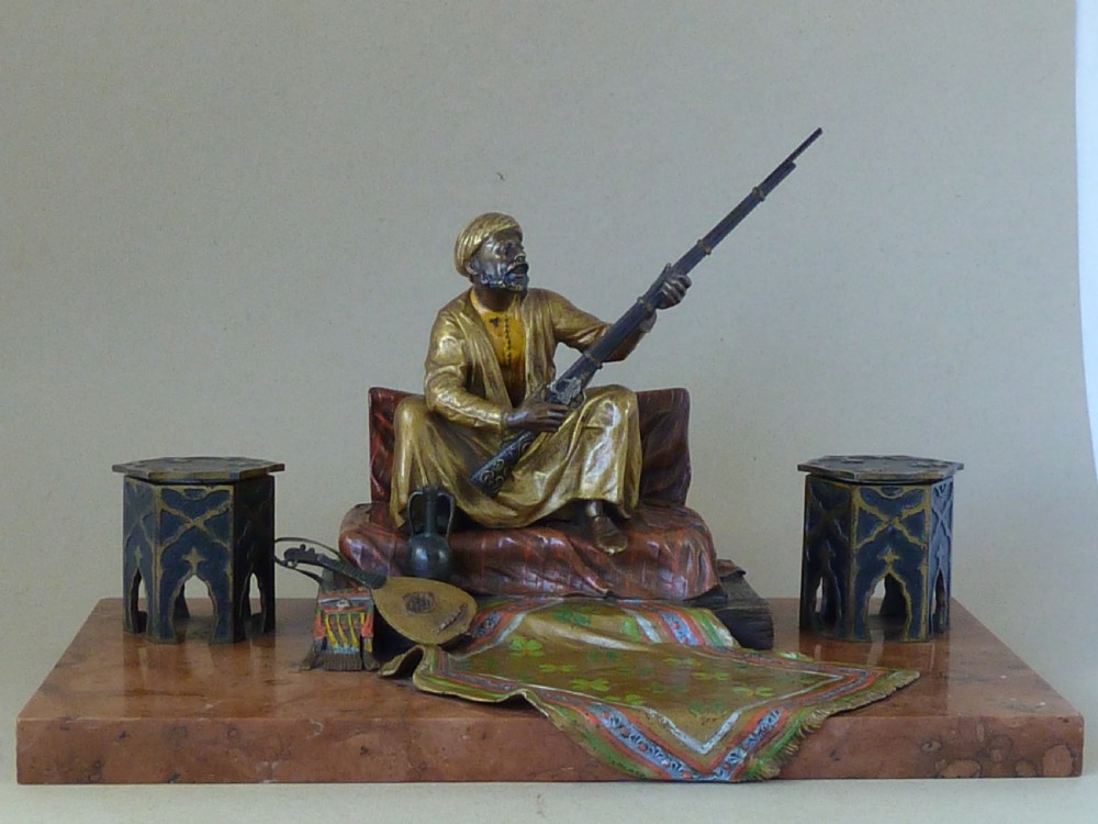 A cold-painted Vienna bronze inkstand featuring a seated figure holding a long firearm mounted on a reddish marble slab alongside twin octagonal inkwell boxes. View II