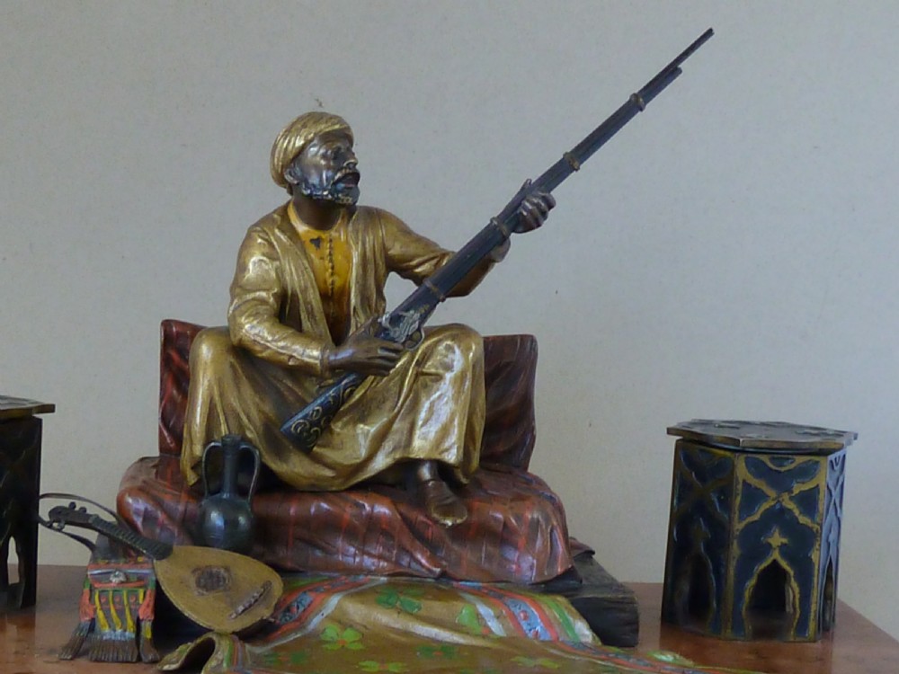 A cold-painted Vienna bronze inkstand featuring a seated figure holding a long firearm mounted on a reddish marble slab alongside twin octagonal inkwell boxes. View III