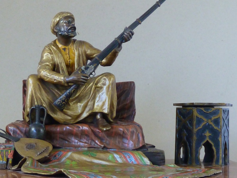 A cold-painted Vienna bronze inkstand featuring a seated figure holding a long firearm mounted on a reddish marble slab alongside twin octagonal inkwell boxes. View IV