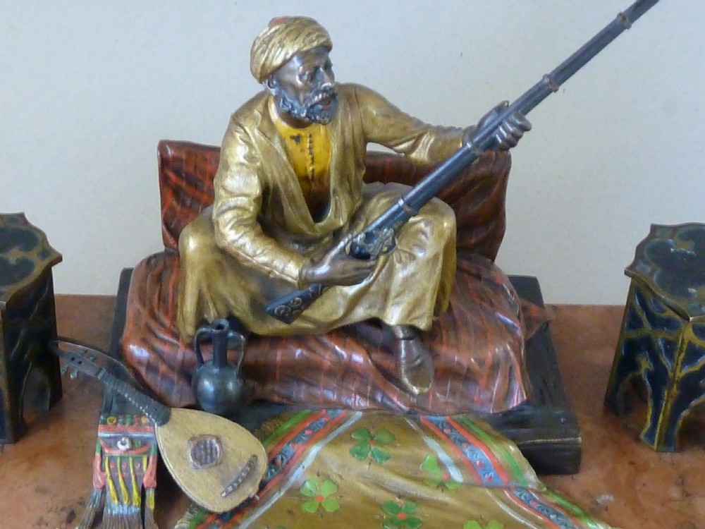 A cold-painted Vienna bronze inkstand featuring a seated figure holding a long firearm mounted on a reddish marble slab alongside twin octagonal inkwell boxes. View VI