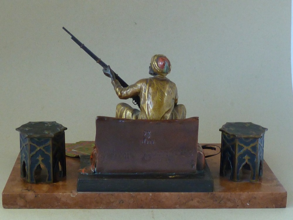 A cold-painted Vienna bronze inkstand featuring a seated figure holding a long firearm mounted on a reddish marble slab alongside twin octagonal inkwell boxes. View VIII