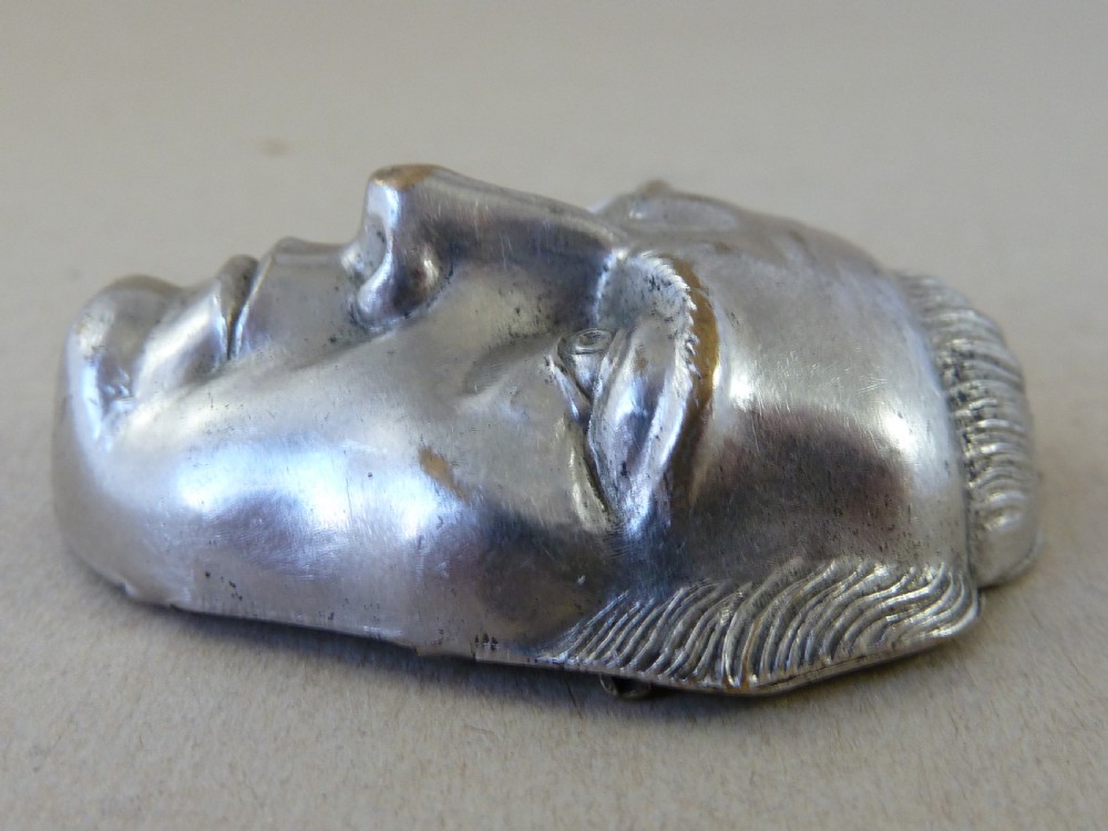 A nickel-plated metal vesta case cast in the high-relief shape of a mans face wearing a monocle. View III