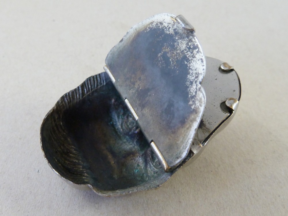 A nickel-plated metal vesta case cast in the high-relief shape of a mans face wearing a monocle. View V