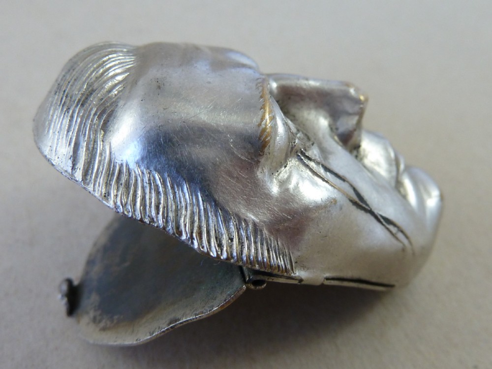 A nickel-plated metal vesta case cast in the high-relief shape of a mans face wearing a monocle. View VI