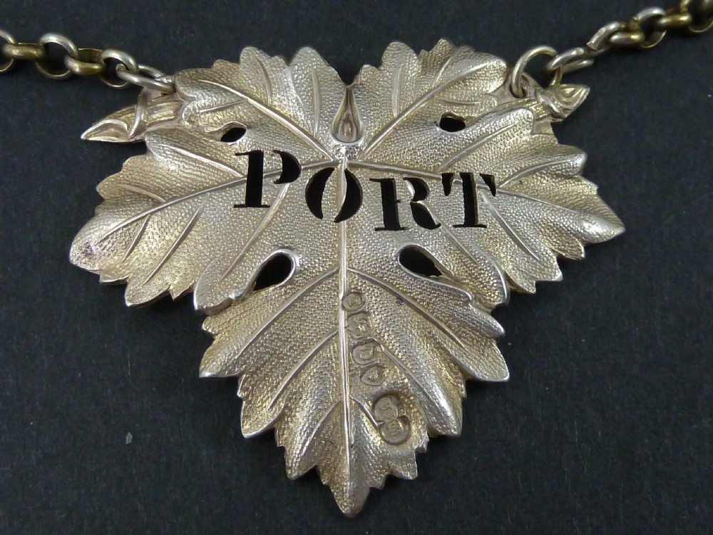 A Victorian sterling silver decanter label shaped as a vine leaf, pierced with the word PORT and attached to a metal suspension chain.