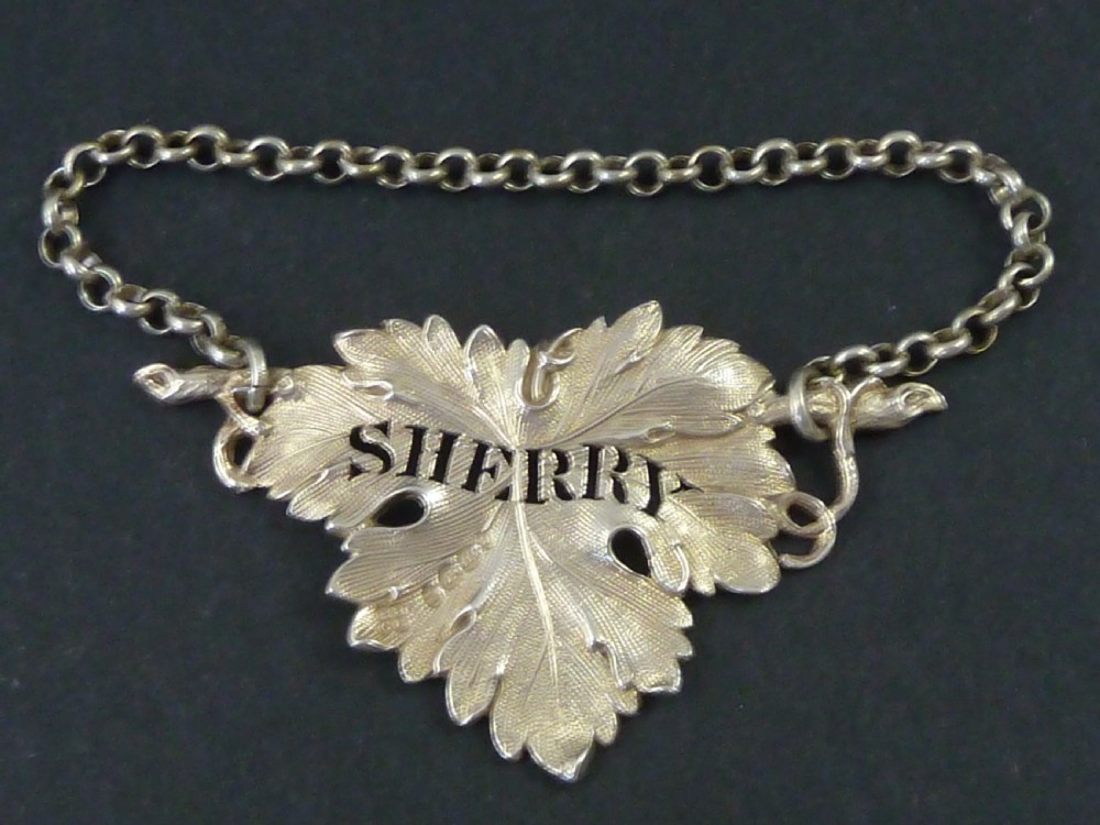 A George IV sterling silver decanter label shaped as a detailed vine leaf with pierced lettering reading SHERRY and attached suspension chain.