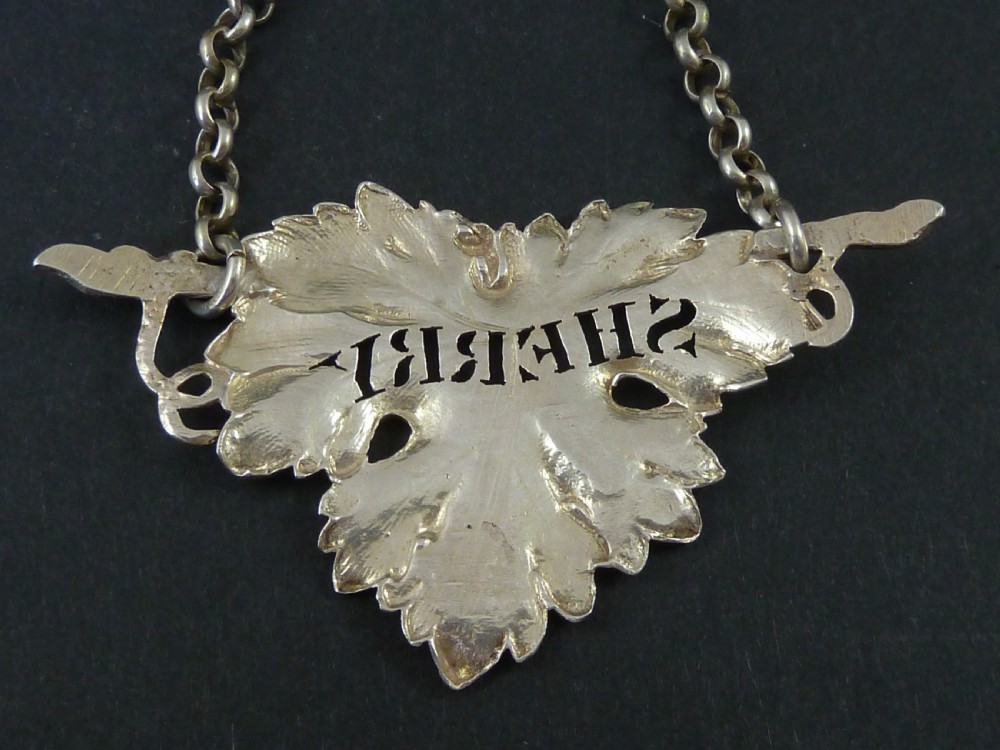 A George IV sterling silver decanter label shaped as a detailed vine leaf with pierced lettering reading SHERRY and attached suspension chain. View IV
