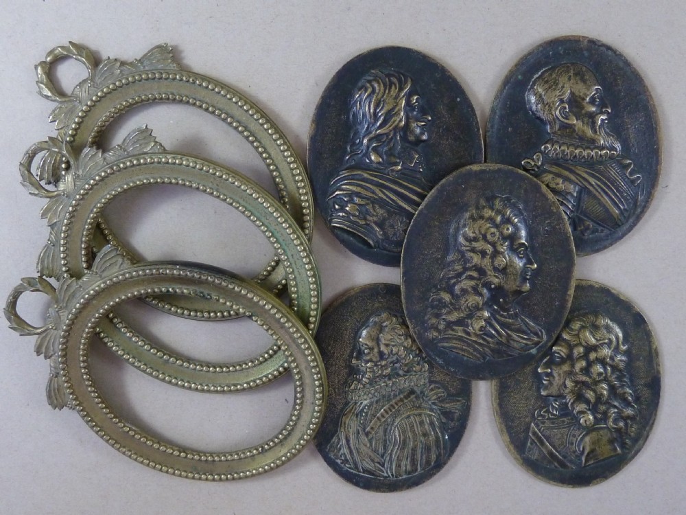 A set of five dark bronze oval portrait medallions depicting historical figures, alongside decorative cast brass frames with bow motifs.