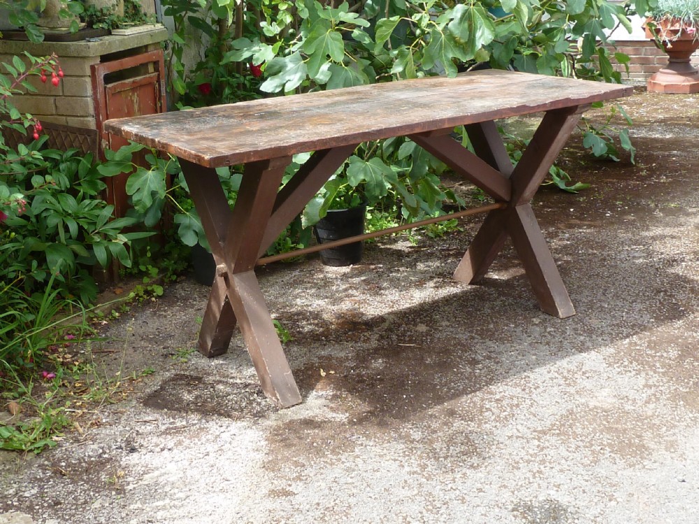 A rustic painted pine tavern table featuring an X-frame trestle base, an iron stretcher rod, and a weathered two-plank top with cleated ends.
