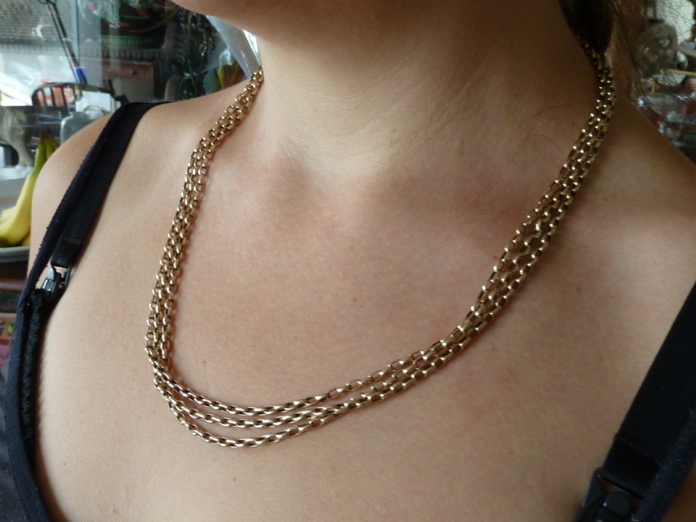A long 14ct yellow gold Victorian guard chain featuring interlocking oval links and a dog clip clasp, laid flat against a neutral surface. View IX