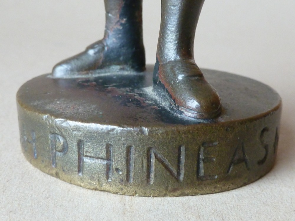 A dark bronze figure depicting a Scottish Highlander in military uniform standing on a circular base inscribed with text. View III