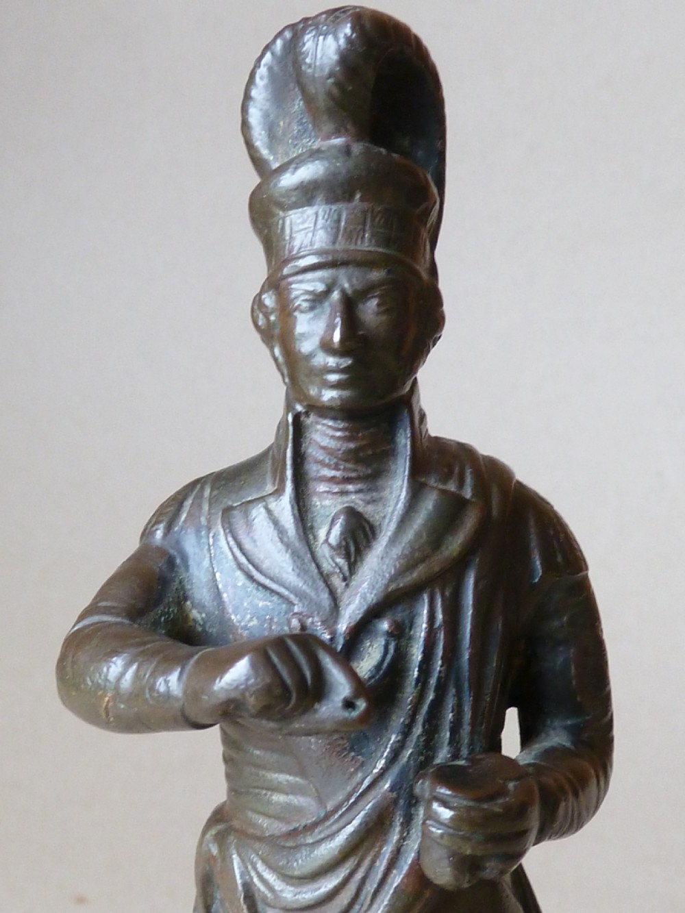 A dark bronze figure depicting a Scottish Highlander in military uniform standing on a circular base inscribed with text. View IV