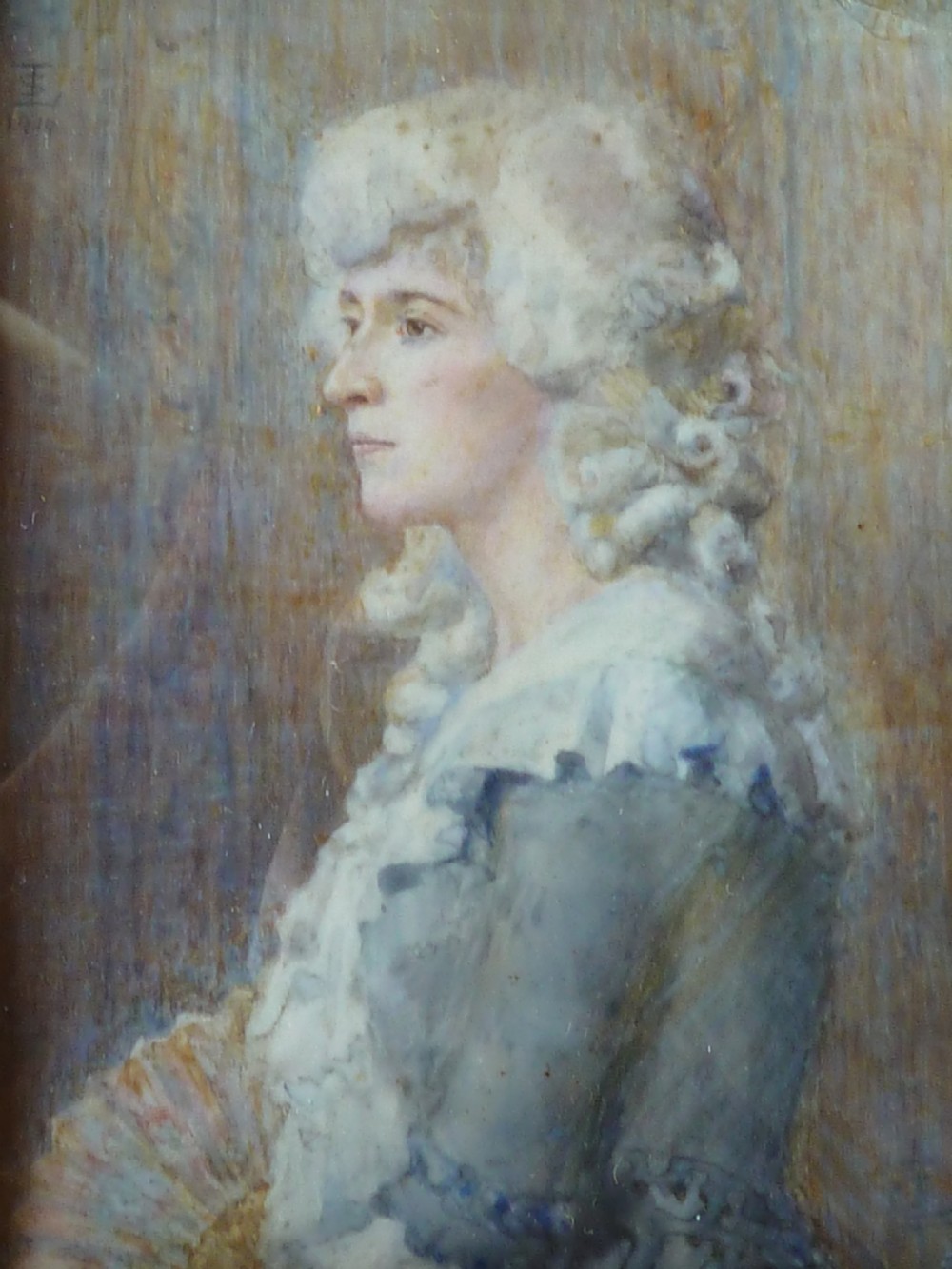A profile portrait miniature painting of a lady in an eighteenth-century style powdered wig and ruffled blue dress, signed and dated 1914.