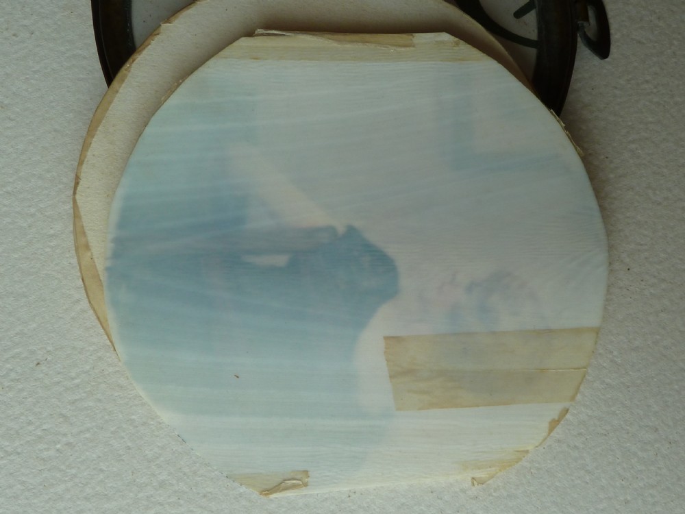 A circular Art Deco hand-painted portrait miniature depicting a 1920s blonde woman in a black dress with a blue wrap, set within an etched circular metal frame. View IV