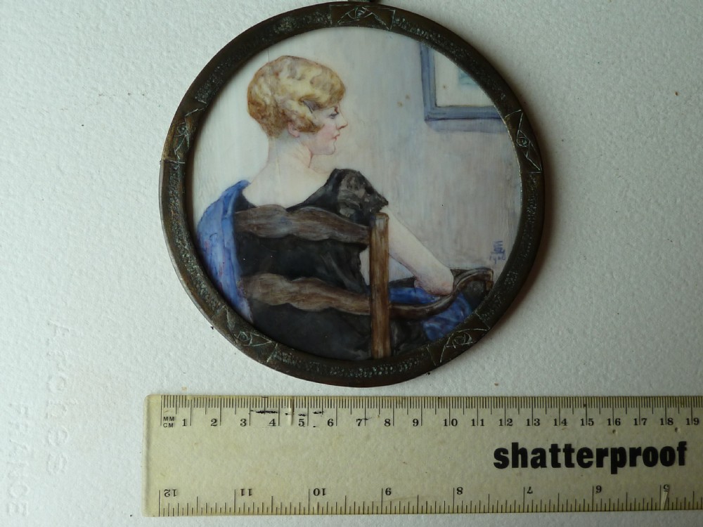 A circular Art Deco hand-painted portrait miniature depicting a 1920s blonde woman in a black dress with a blue wrap, set within an etched circular metal frame. View VI