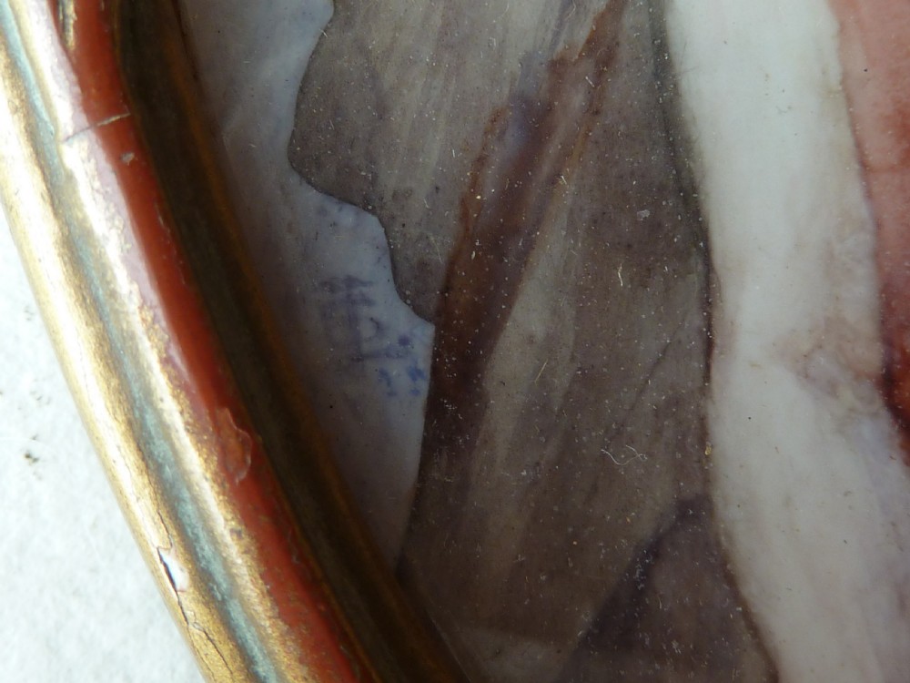 An oval Art Deco portrait miniature depicting a woman with short dark hair in a pinkish-terracotta dress, housed within a twisted metal frame. View IV