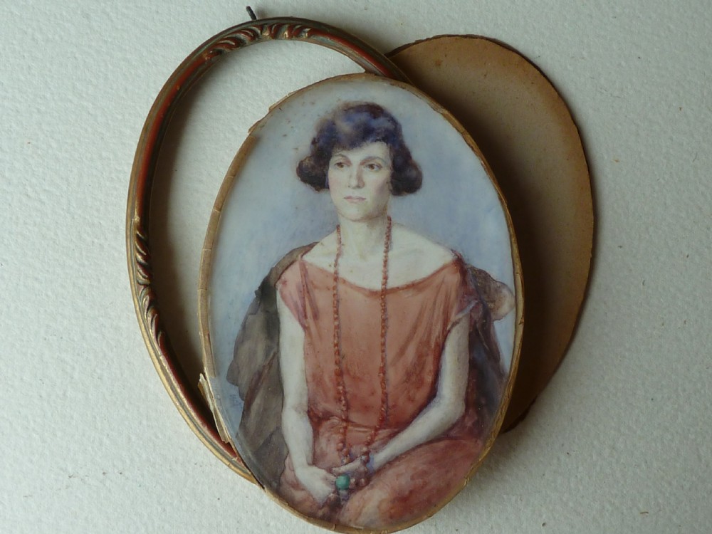 An oval Art Deco portrait miniature depicting a woman with short dark hair in a pinkish-terracotta dress, housed within a twisted metal frame. View VI