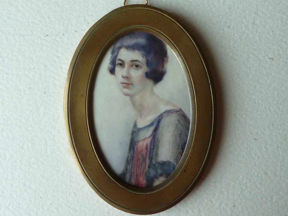 An oval Art Deco portrait miniature depicting a woman with short dark bobbed hair set in a plain brass frame.