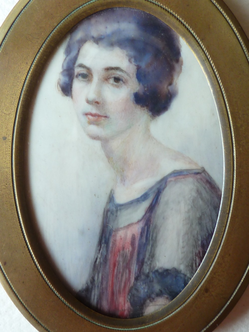 An oval Art Deco portrait miniature depicting a woman with short dark bobbed hair set in a plain brass frame. View II