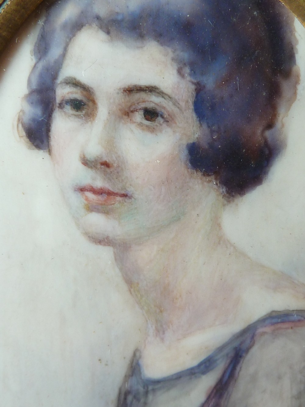 An oval Art Deco portrait miniature depicting a woman with short dark bobbed hair set in a plain brass frame. View III