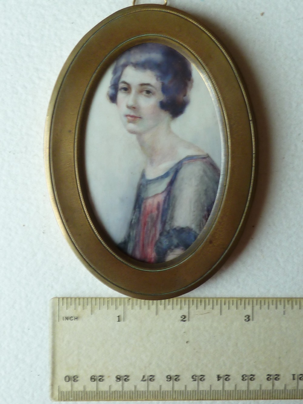 An oval Art Deco portrait miniature depicting a woman with short dark bobbed hair set in a plain brass frame. View V