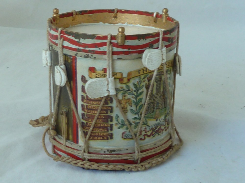 A miniature painted regimental snare drum with rope tensioning enclosed within a brass-bound glass display case on a dark timber base. View VI