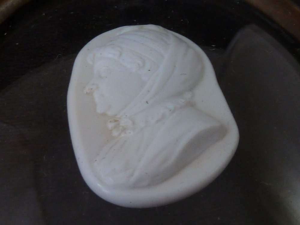 A Georgian oval white glass paste profile bust miniature mounted in a brass bezel on a rectangular black ebonised wooden plaque with a brass acorn hanger. View V