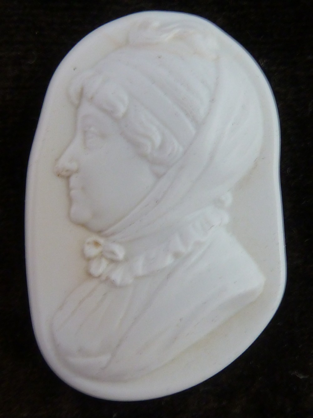 A Georgian oval white glass paste profile bust miniature mounted in a brass bezel on a rectangular black ebonised wooden plaque with a brass acorn hanger. View VI