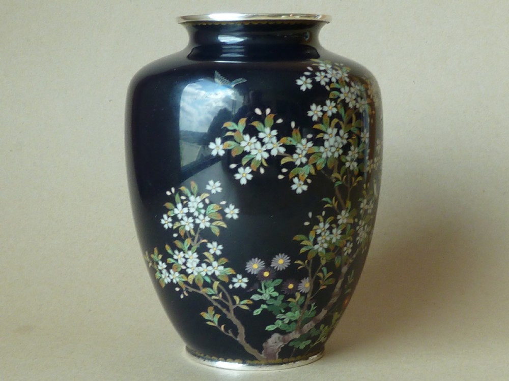 A black Japanese cloisonne enamel vase decorated with silver wire depicting white blossoms, foliage, and birds, finished with silver rim and foot rim.