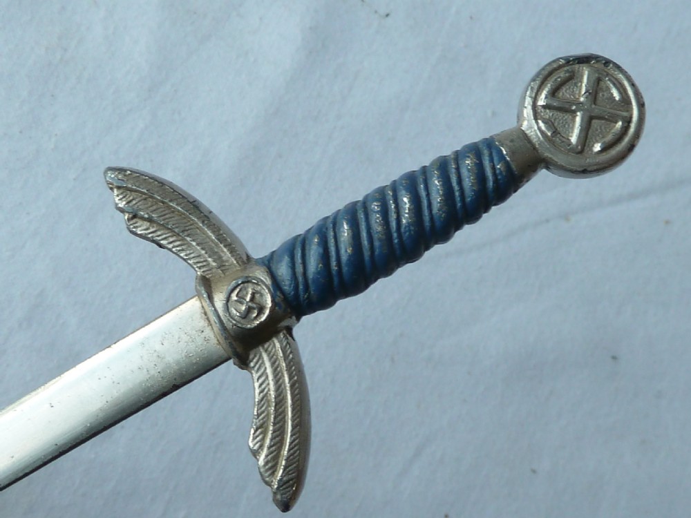 A miniature dagger letter opener featuring a tapered steel blade, down-swept crossguard, ribbed blue handle, and circular pommel. View III