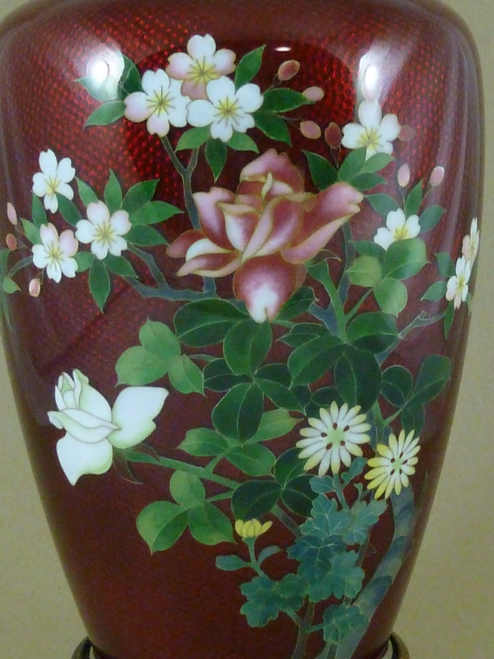 A red Japanese ginbari enamel vase decorated with floral silver wire motifs set upon a dark carved wooden base. View II