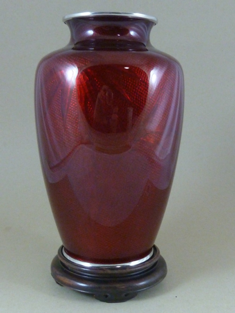 A red Japanese ginbari enamel vase decorated with floral silver wire motifs set upon a dark carved wooden base. View III