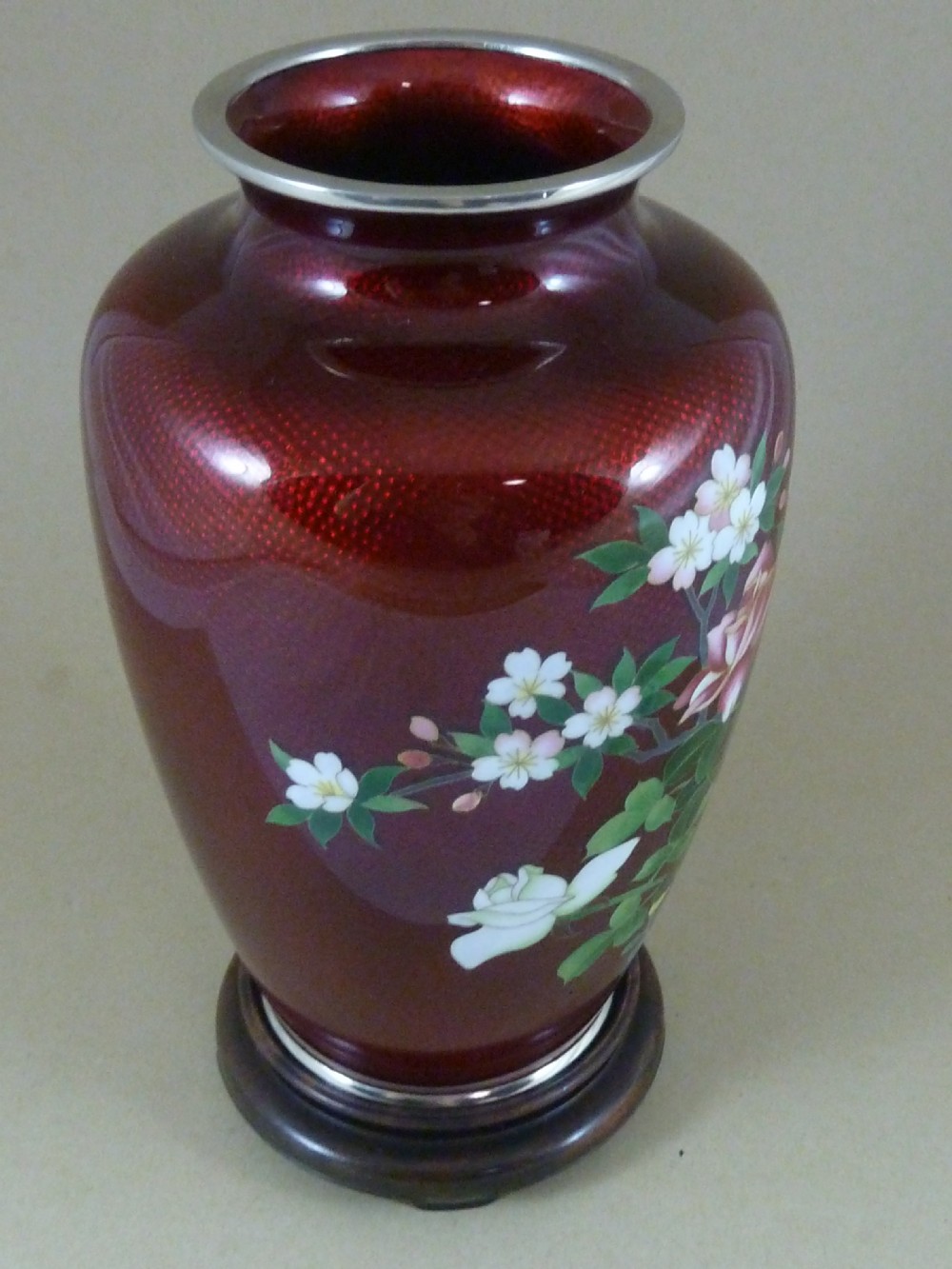 A red Japanese ginbari enamel vase decorated with floral silver wire motifs set upon a dark carved wooden base. View V