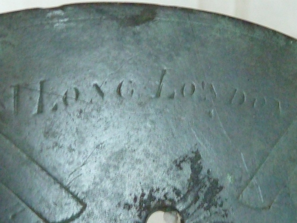 A circular weathered bronze sundial plate with a central triangular gnomon, engraved Roman numerals, and a green verdigris patina. View V