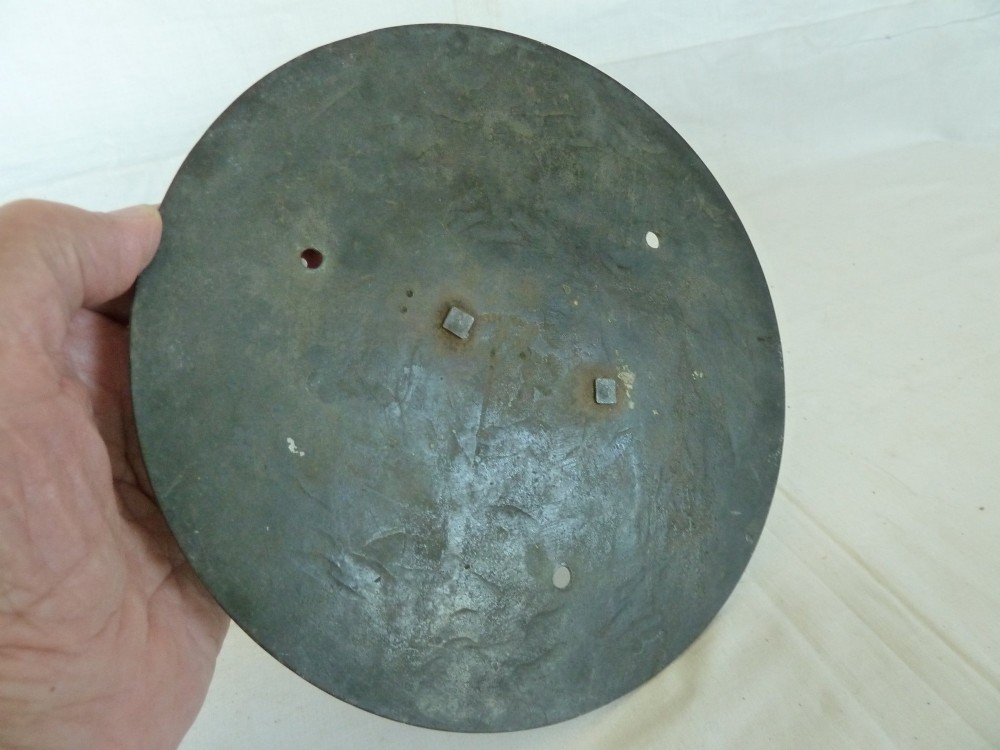 A circular weathered bronze sundial plate with a central triangular gnomon, engraved Roman numerals, and a green verdigris patina. View VII