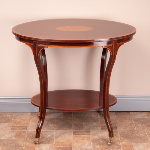 fig 1. An Edwardian oval mahogany occasional table featuring a central marquetry medallion, satinwood crossbanding, lower undertier, and splayed legs with brass castors.