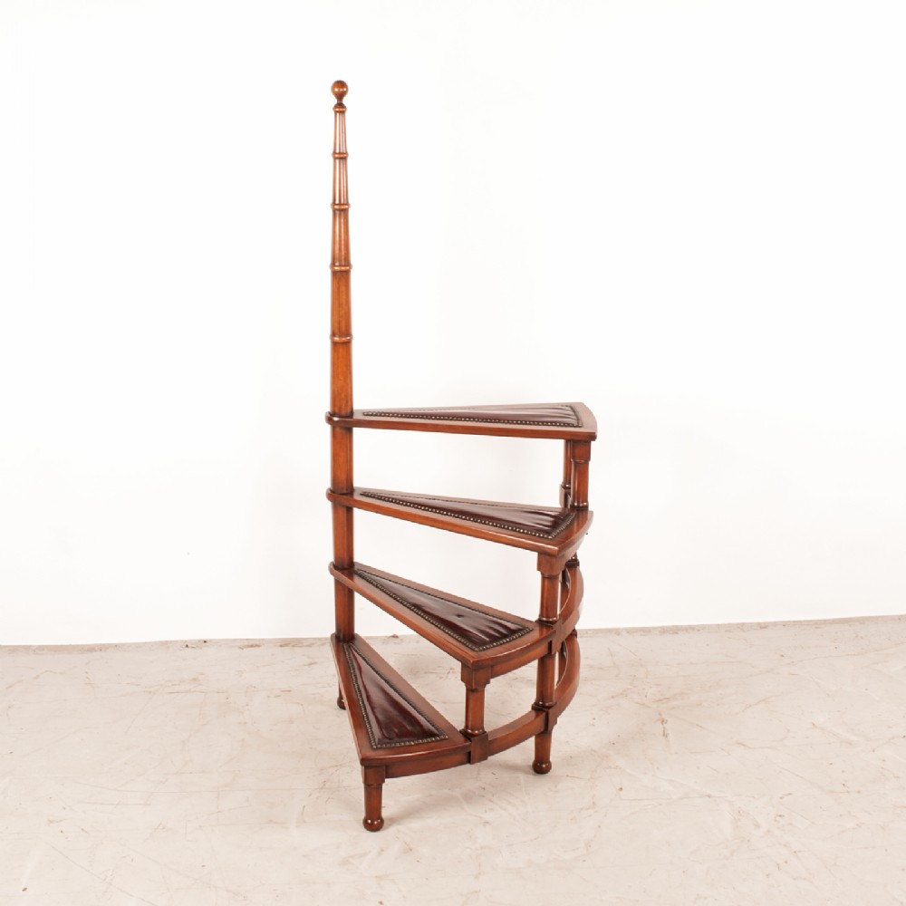 A spiral set of dark mahogany library steps with four leather-lined triangular treads and a central turned handrail post.