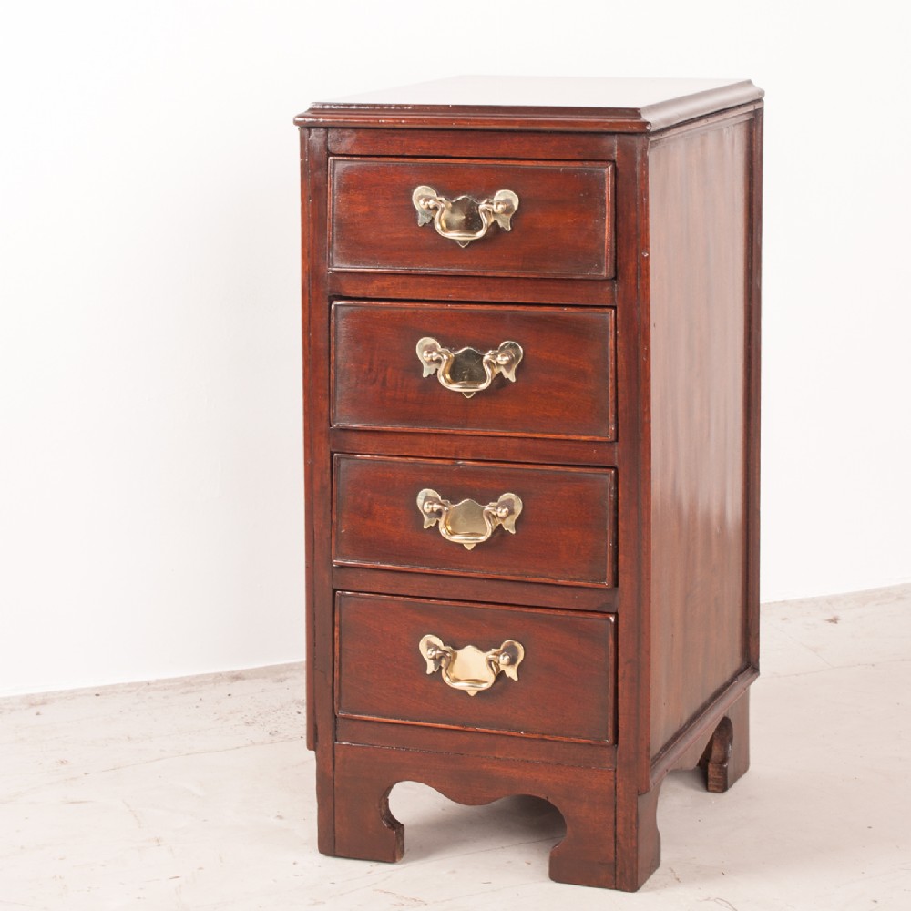 A narrow dark brown mahogany chest featuring four stacked drawers with polished brass drop handles and a shaped bracket foot apron.