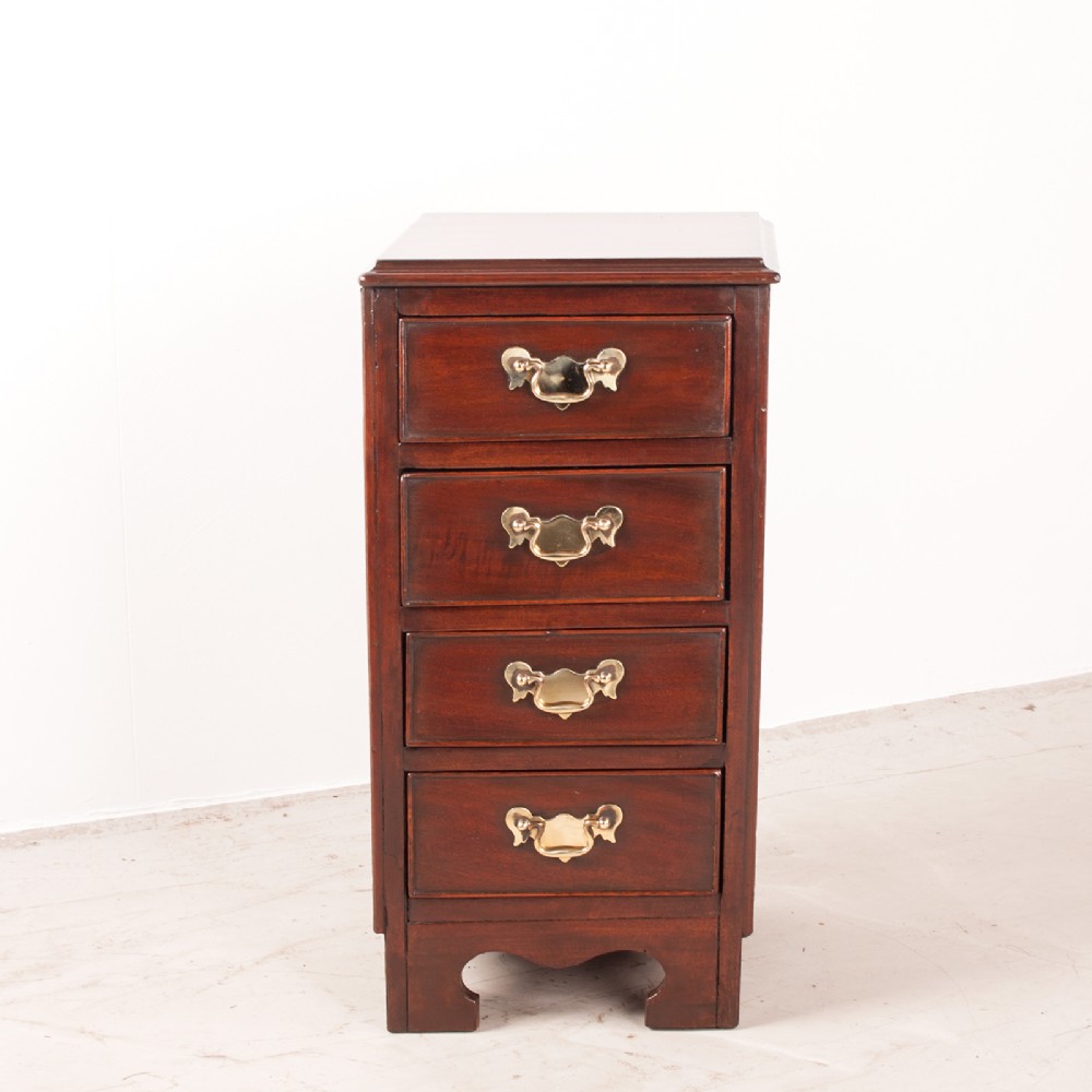 A narrow dark brown mahogany chest featuring four stacked drawers with polished brass drop handles and a shaped bracket foot apron. View II