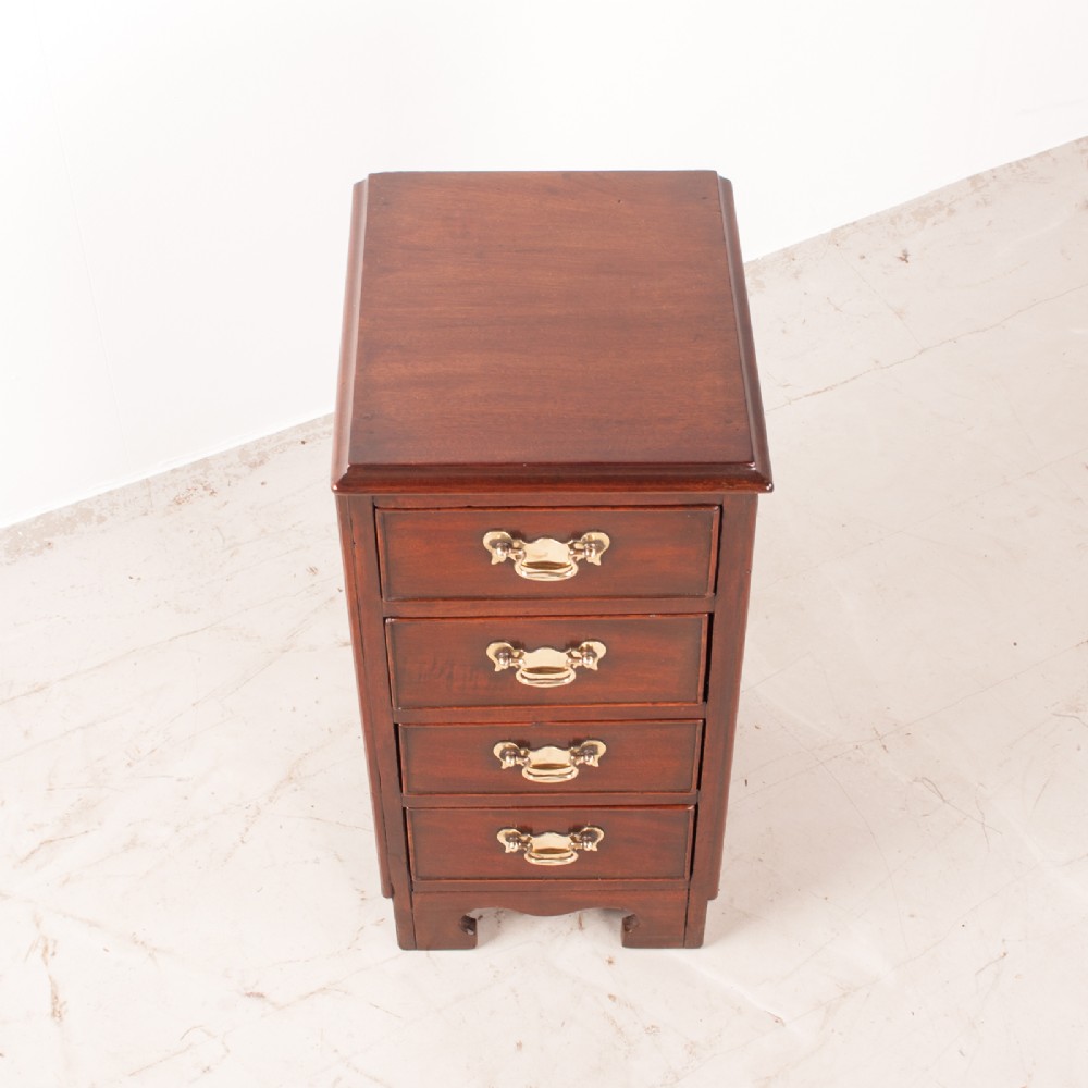 A narrow dark brown mahogany chest featuring four stacked drawers with polished brass drop handles and a shaped bracket foot apron. View III