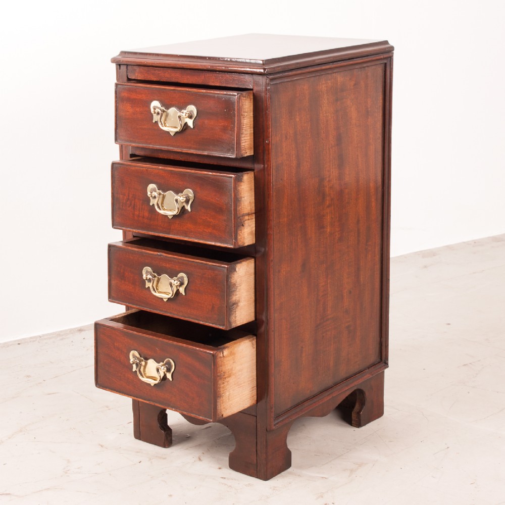 A narrow dark brown mahogany chest featuring four stacked drawers with polished brass drop handles and a shaped bracket foot apron. View IV