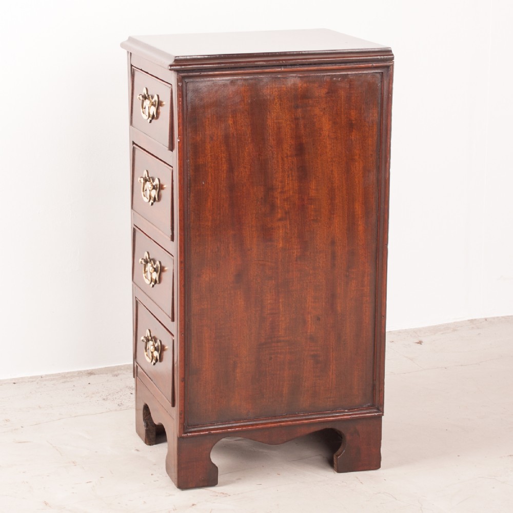 A narrow dark brown mahogany chest featuring four stacked drawers with polished brass drop handles and a shaped bracket foot apron. View VI