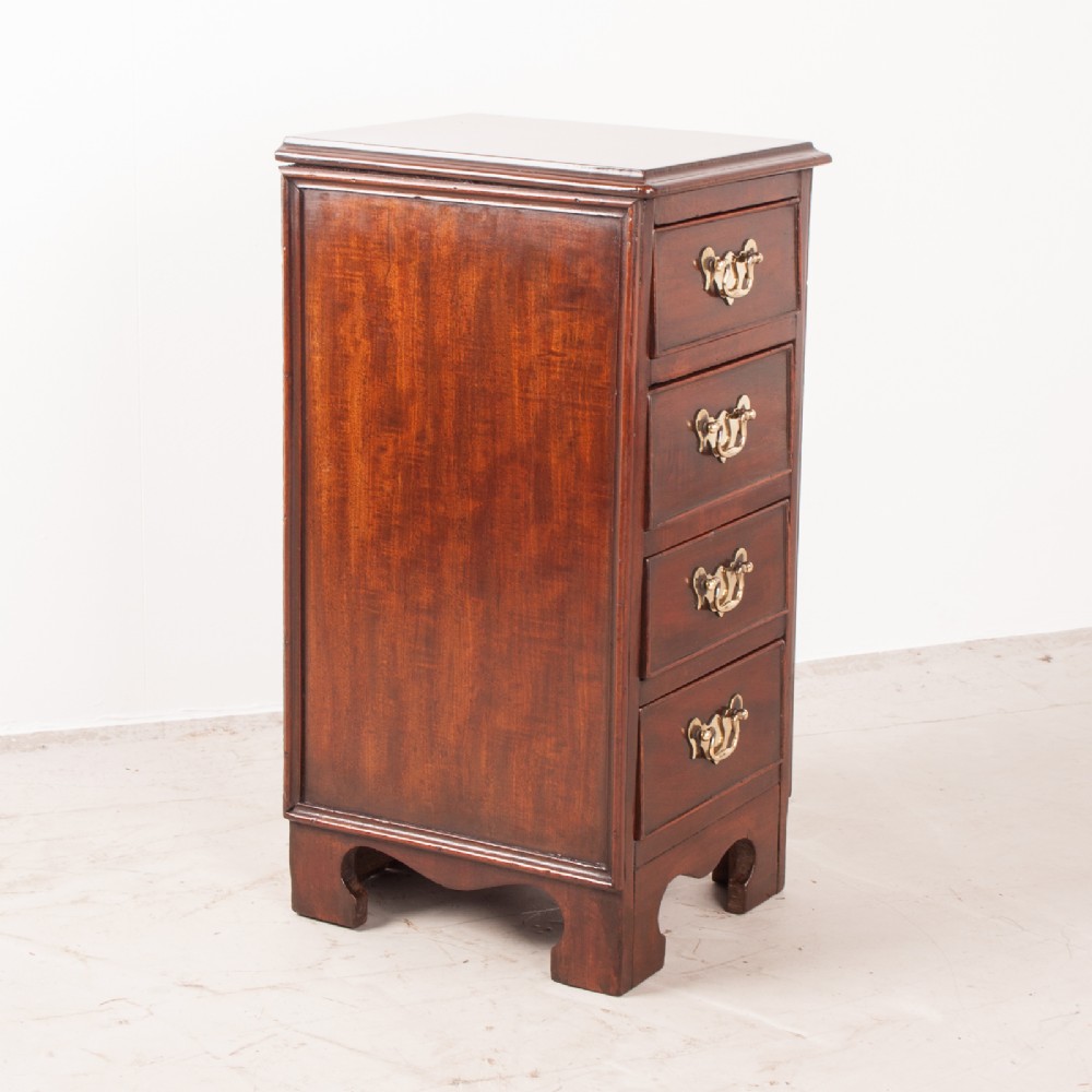 A narrow dark brown mahogany chest featuring four stacked drawers with polished brass drop handles and a shaped bracket foot apron. View VII