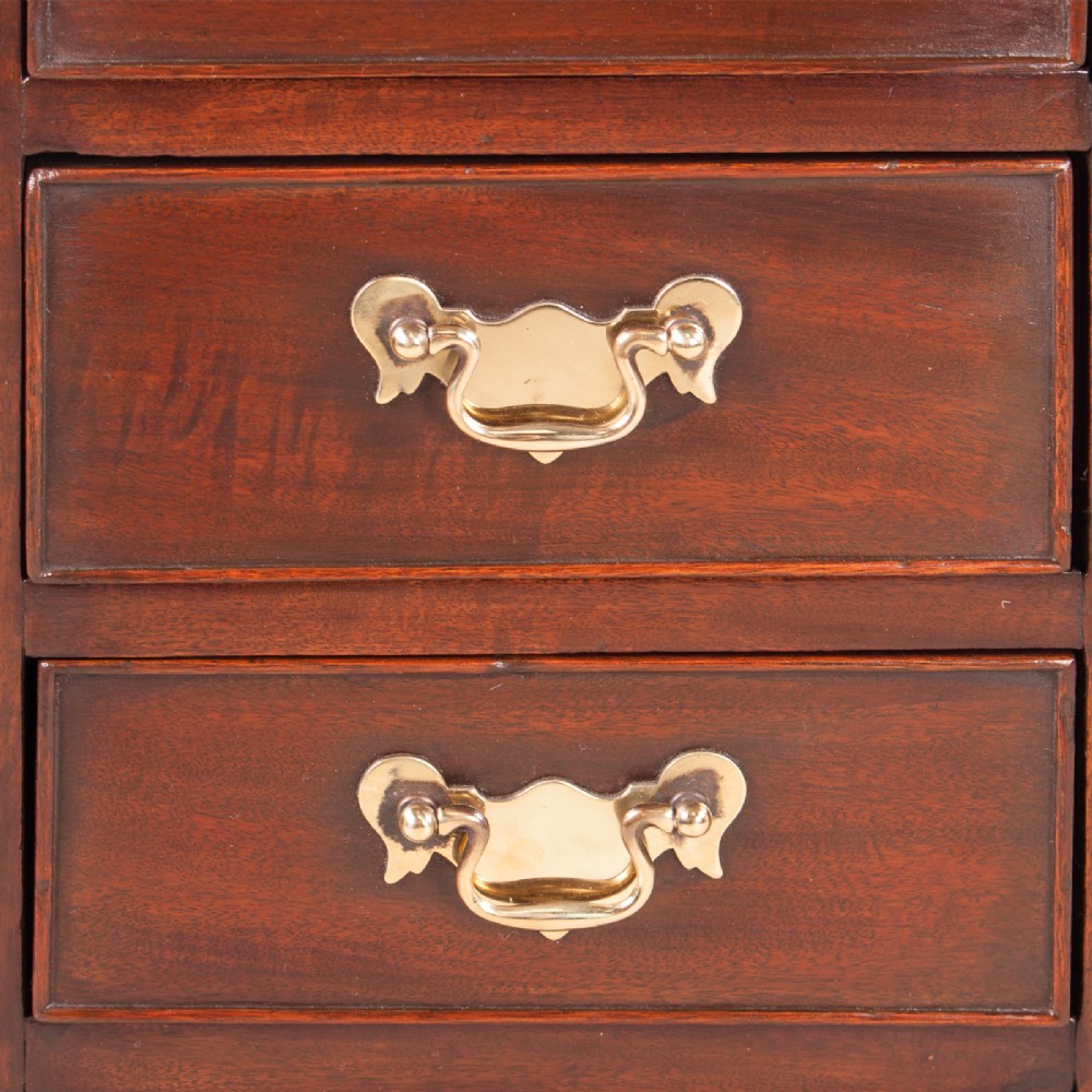 A narrow dark brown mahogany chest featuring four stacked drawers with polished brass drop handles and a shaped bracket foot apron. View VIII