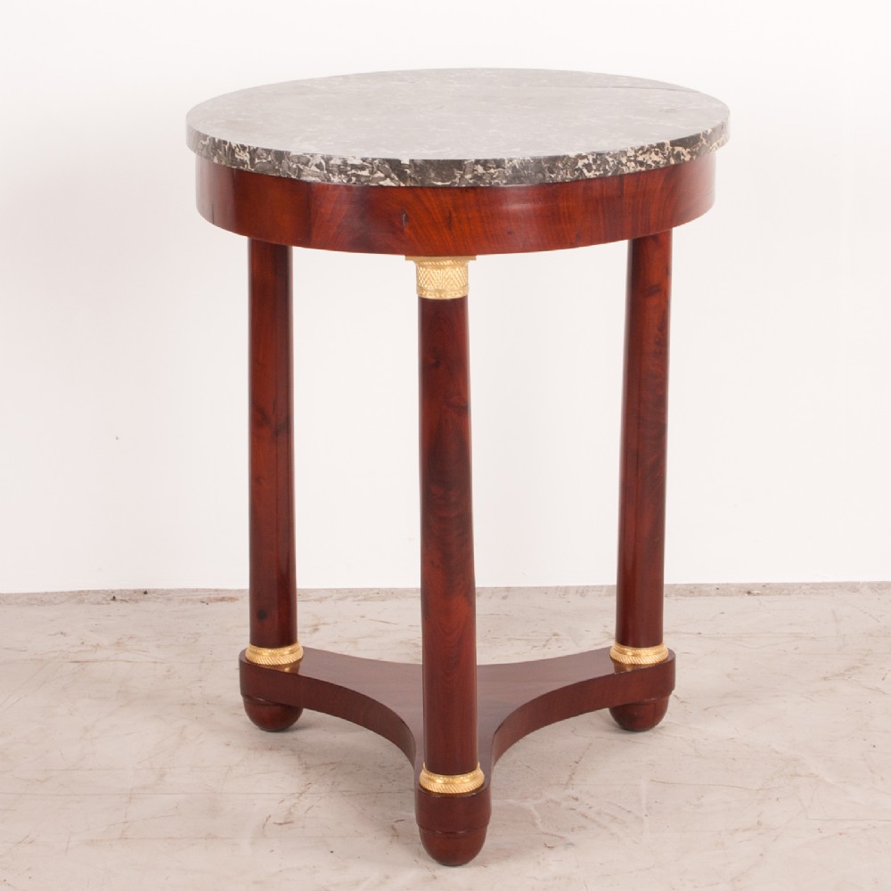 A 19th-century French mahogany gueridon side table with a round grey marble top, three cylindrical legs with gilt mounts, and a tri-form concave base. View II