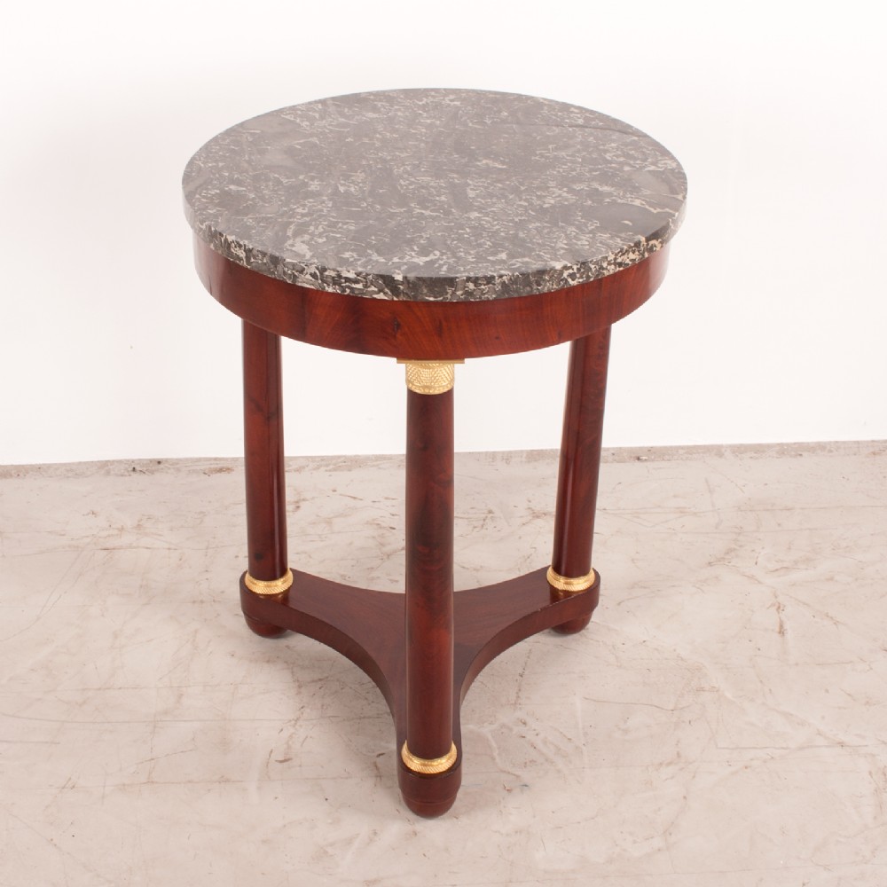 A 19th-century French mahogany gueridon side table with a round grey marble top, three cylindrical legs with gilt mounts, and a tri-form concave base. View III