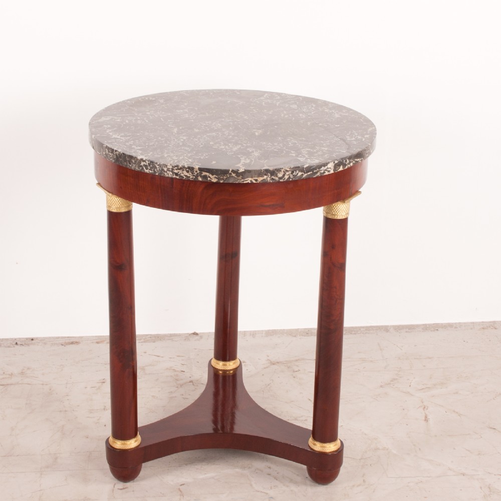 A 19th-century French mahogany gueridon side table with a round grey marble top, three cylindrical legs with gilt mounts, and a tri-form concave base. View IV