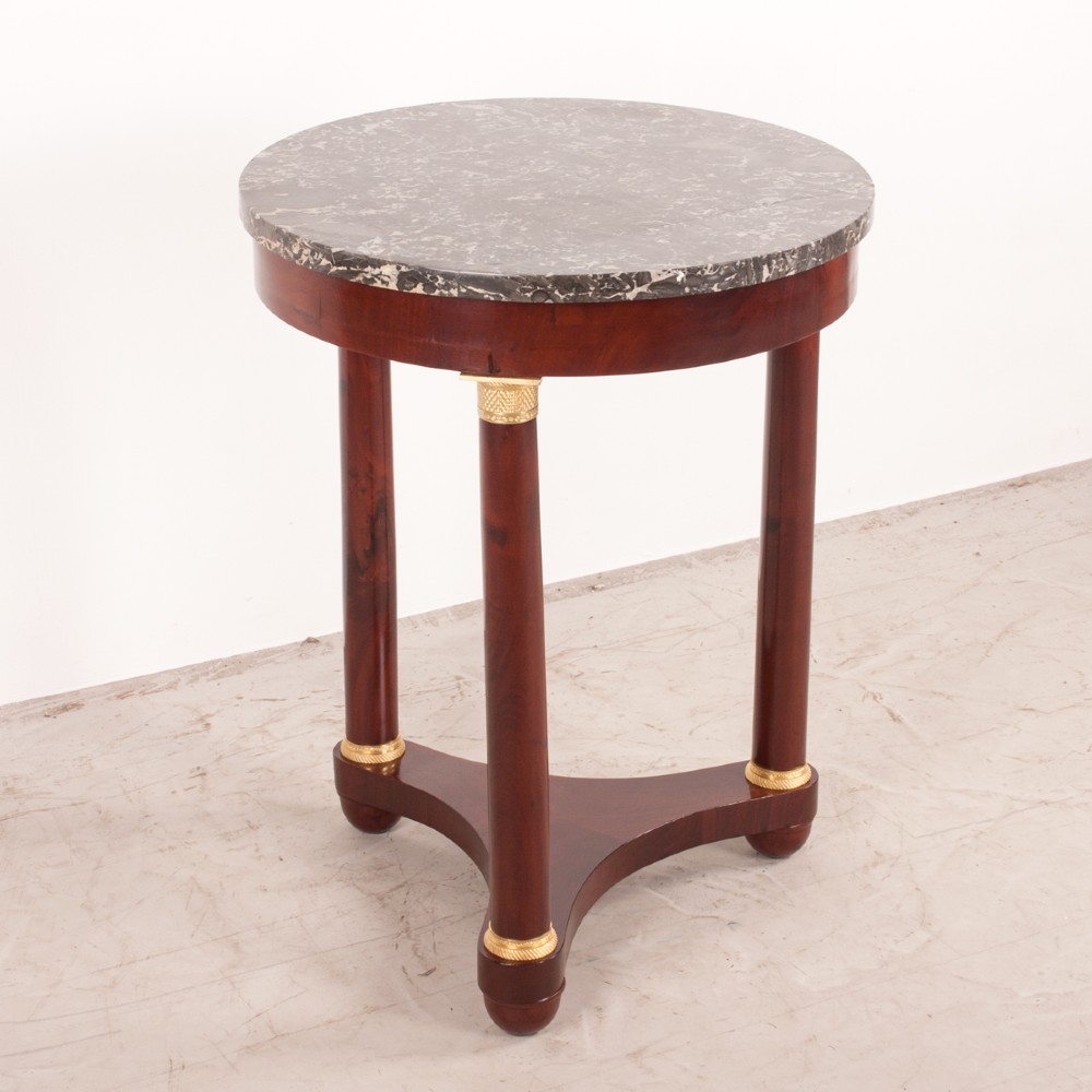 A 19th-century French mahogany gueridon side table with a round grey marble top, three cylindrical legs with gilt mounts, and a tri-form concave base. View V
