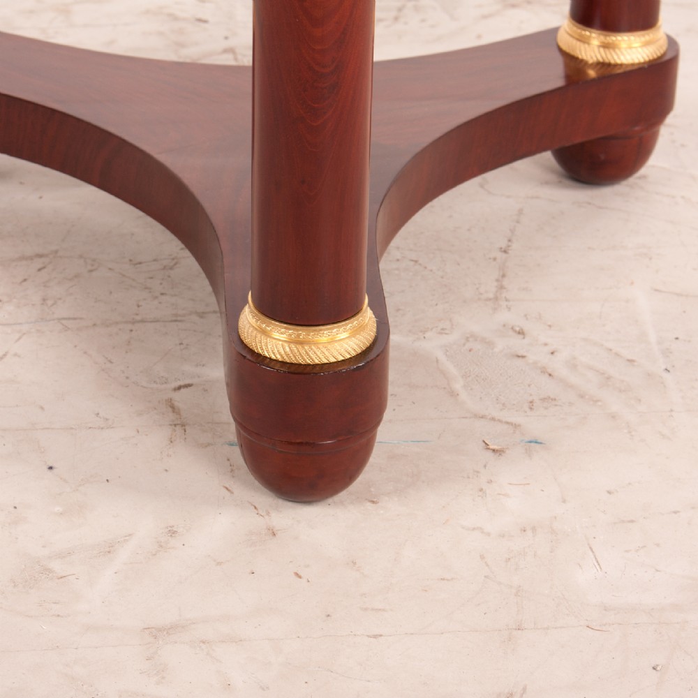 A 19th-century French mahogany gueridon side table with a round grey marble top, three cylindrical legs with gilt mounts, and a tri-form concave base. View VI